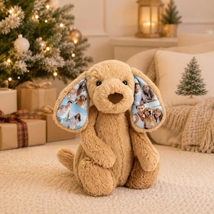 Puede incluir: Un juguete de peluche con forma de perro en color beige, con pelaje suave, nariz marrón oscuro y orejas caídas. El interior de cada oreja presenta un collage de fotos personalizado impreso en la tela, mostrando imágenes de personas y un perro.
