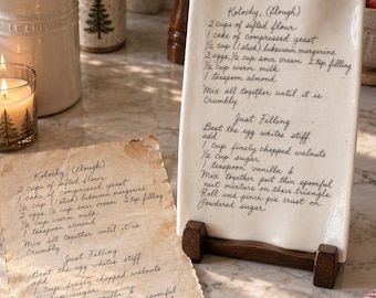 May include: A rectangular white ceramic plaque on a dark wooden stand, featuring a handwritten recipe for Kolochy. The text lists ingredients like sifted flour, yeast, margarine, eggs, sour cream, milk, almond, walnuts, sugar, and vanilla.