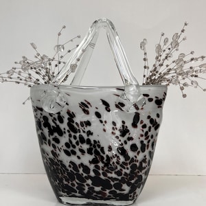 May include: A white ceramic mug with a black handle and the text "But First, Coffee" in a black, handwritten-style font. The mug is on a white surface.