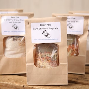 May include: Four brown paper bags with clear plastic windows, each containing a different soup mix. The bags are labeled "Bear Paw" and have the text "Corn Chowder Soup Mix" and "Cranberry Orange Biscuit and Scone Mix".
