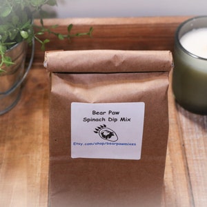 May include: A brown paper bag with a white label that says "Bear Paw Spinach Dip Mix" and a website address. The bag is sitting on a wooden surface.