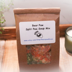 May include: A brown paper bag with a clear window showing split pea soup mix. The bag has a white label that says "Bear Paw Split Pea Soup Mix" and a website address.