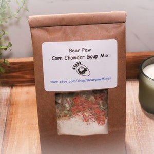 May include: A brown paper bag with a clear window showing a corn chowder soup mix. The bag has a white label with the text "Bear Paw Corn Chowder Soup Mix" and a paw print logo. The website address "www.etsy.com/shop/BearpawMixes" is printed below the logo.