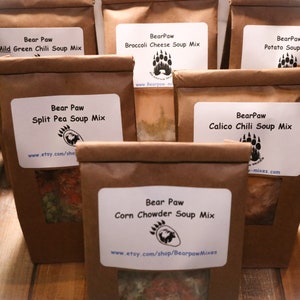 May include: Six brown paper bags with white labels, each containing a different soup mix. The labels feature the text "Bear Paw" and the name of the soup mix, such as "Split Pea Soup Mix" and "Calico Chili Soup Mix".
