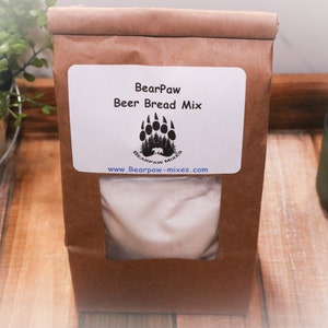 May include: A brown paper bag with a white label that says "BearPaw Beer Bread Mix" and a black bear paw logo. The bag contains a white powder mix.