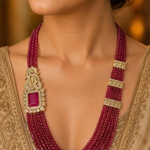 May include: A multi-strand necklace featuring deep magenta beads, accented with gold-toned rectangular spacers set with clear stones and a large, rectangular magenta pendant framed by intricate gold-toned metalwork and clear stones.