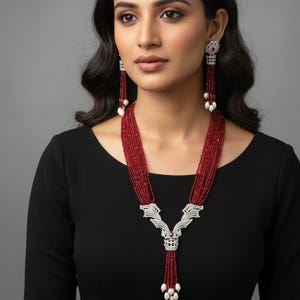 May include: A red beaded necklace and matching earrings set. The necklace features a detailed silver pendant with a red gemstone accent and white pearl drops. The earrings have a similar design with long red bead strands and pearl accents.