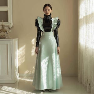 Peut inclure: Un haut noir à col montant avec des volants aux épaules est associé à une jupe longue bleu clair. La tenue a un aspect brillant en cuir verni. Le modèle se tient dans une pièce bien éclairée avec une armoire blanche et une fenêtre en arrière-plan.
