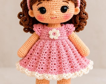 May include: A handcrafted crochet doll with brown curly hair, wearing a pink dress with a white flower accent, a matching pink headband with a bow and flower, and pink shoes with white flower details. The doll has large black eyes and rosy cheeks.