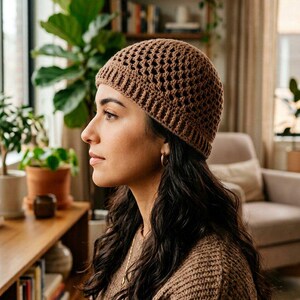 May include: A brown crochet beanie featuring a textured, open-work diamond pattern on the crown and a ribbed, solid-stitch brim. The hat is constructed from a medium-weight yarn and sits snugly on the head, providing a consistent, uniform colour.