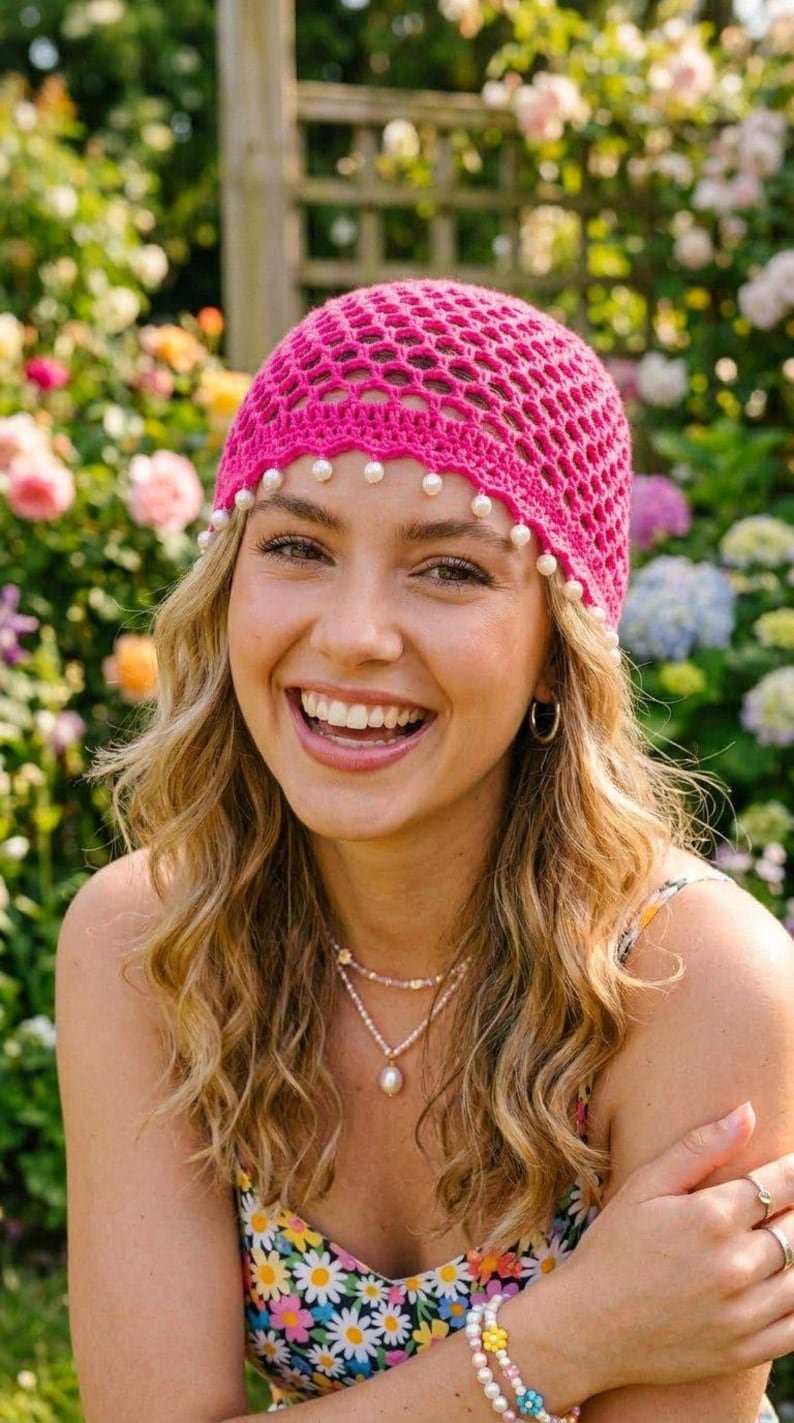 May include: A bright pink crochet beanie featuring an open-weave mesh pattern and a scalloped bottom edge adorned with small, round white faux pearls hanging along the perimeter of the cap, providing a textured and decorative finish to the headwear.