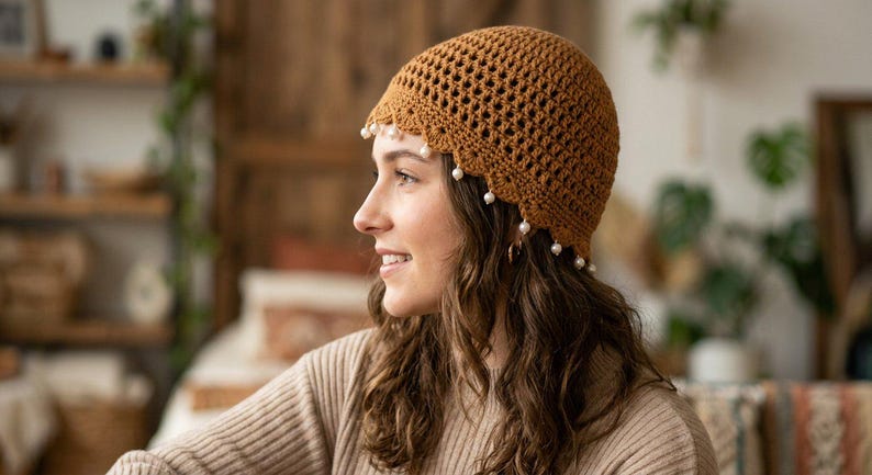 May include: A brown crocheted beanie featuring an openwork lattice pattern throughout the crown and a scalloped edge along the bottom. Small, round, white beads are attached at intervals along the scalloped hem of the hat.