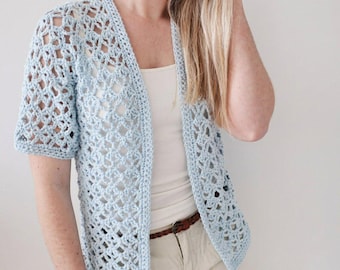 May include: A light blue crochet cardigan featuring an openwork diamond pattern, short sleeves, and a straight front opening. The garment is crafted with a textured yarn and finished with a solid border along the edges, providing a lightweight layer.