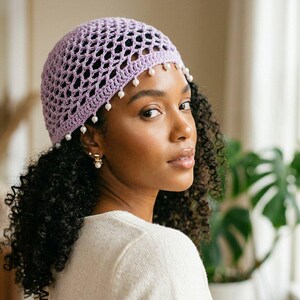 May include: A light purple crochet beanie featuring an open-knit mesh pattern and a decorative border of small white beads dangling along the bottom edge. The hat is constructed from yarn and fits snugly around the crown of the head.