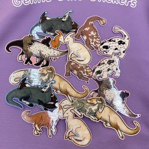 Peut inclure: Une collection d'autocollants de dinosaures de différentes couleurs et motifs, dont blanc, marron et noir, est disposée sur un fond violet. Le texte "Gentle Dino Stickers" est affiché en blanc, en arc de cercle en haut.