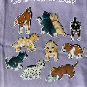 May include: A collection of colorful dog stickers on a lavender background. The stickers feature various dog breeds, including a Shiba Inu, Dalmatian, and Labrador, with playful designs and the text "Cute Dog Stickers" in white.