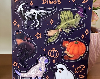 May include: A sticker sheet with the text "HALLOWEEN DINOS" and illustrations of dinosaurs in Halloween costumes. The dinosaurs include a skeleton, a witch, a bat, a pumpkin, a mummy, and a ghost. The background is dark purple with orange stars and diamonds.