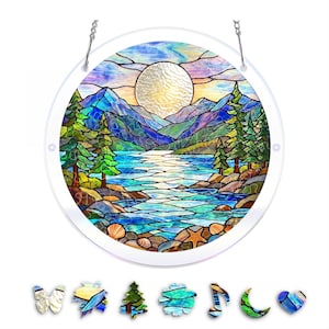 May include: Round stained glass panel depicting a serene lake scene with mountains, trees, and a large sun. The panel is framed in clear glass and hangs from a chain. Includes decorative glass shapes of a butterfly, leaf, tree, flower, musical note, crescent moon, and heart.