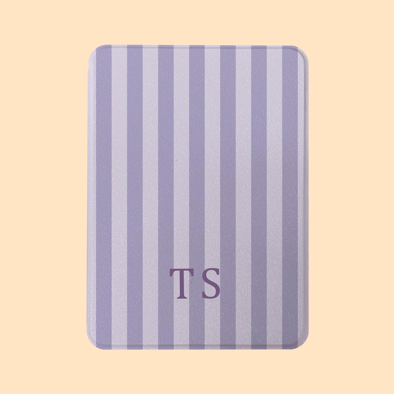 May include: A rectangular, lavender and white striped item with rounded corners. The item has the initials "TS" in the center. The background is a solid, light peach color.