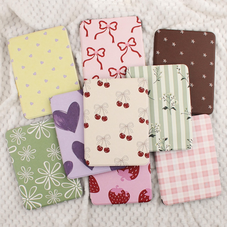 Puede incluir: Una colecci&oacute;n de cuadernos rectangulares con varios dise&ntilde;os. Los dise&ntilde;os incluyen lazos rosas, cerezas, fresas, corazones, flores y cuadros vichy. Los colores incluyen rosa, amarillo, verde, morado y marr&oacute;n. Los cuadernos est&aacute;n colocados sobre una superficie blanca texturizada.