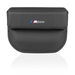 Puede incluir: Un organizador de asiento de coche negro con el logotipo de BMW M. El organizador tiene una sección superior rectangular y una sección inferior curva. El logotipo de BMW M es azul, rojo y blanco. El organizador es de material liso.