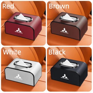 K&ouml;nnte beinhalten: Vier Taschentuchboxen in Rot, Braun, Wei&szlig; und Schwarz. Jede Box hat eine silberfarbene ovale &Ouml;ffnung zur Taschentuchausgabe und ein Mitsubishi-Logo. Die Boxen sind rechteckig mit abgerundeten Kanten.