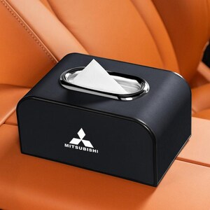 K&ouml;nnte beinhalten: Schwarze Taschentuchbox mit silberner Zierleiste und Mitsubishi-Logo. Wei&szlig;e Taschent&uuml;cher sind sichtbar. Die Box steht auf einer braunen Oberfl&auml;che.