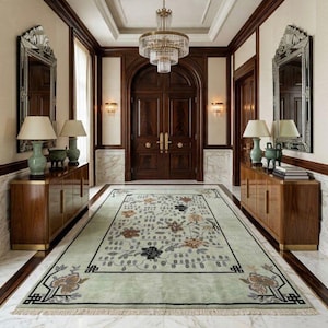 May include: An elegant entryway featuring a light green floral rug with a black border, flanked by matching wooden cabinets with lamps and mirrors. A large chandelier hangs above the rug, and a dark wood door is at the end of the hallway.