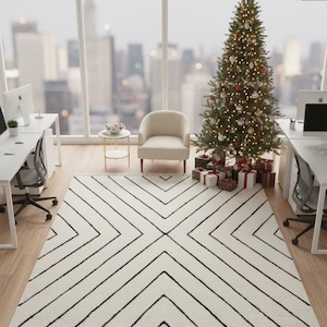 Puede incluir: Una oficina moderna con un árbol de Navidad, regalos y una alfombra geométrica. La alfombra es blanca con líneas negras y flecos. Una silla blanca y una mesa pequeña están cerca de la ventana. Se ven escritorios y computadoras.