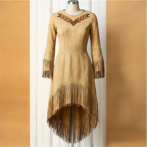 May include: A tan suede dress featuring long sleeves with fringe trim at the cuffs, a high-low hemline with extensive fringe detailing, and a V-shaped geometric pattern in brown, orange, and black tones across the upper chest area.