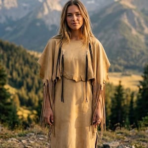 Può includere: Un abito in camoscio color marrone chiaro con un corpetto a strati in stile mantella con lunghe frange lungo l'orlo e le maniche. Il capo include sottili lacci in pelle nera che pendono dallo scollo e una gonna dritta con frange sul fondo.