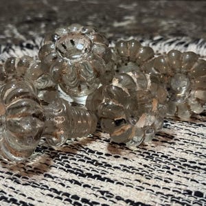 以下が含まれることがあります： 花柄のデザインが施された透明なガラス製のキャビネットノブのコレクション。ノブは白黒の模様の生地の上に配置されています。ノブはリブ状のテクスチャで、取り付け用のネジが付いています。