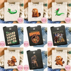 May include: Collection of t-shirts and sweatshirts featuring cartoon characters and the word "HOPPERS". Designs include a green lizard, a brown beaver, and a group of characters. The shirts are in various colors, including cream and black.