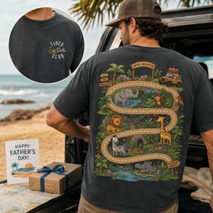 May include: A charcoal gray t-shirt featuring a small front chest graphic that reads "TIRED Dads CLUB" and a large back graphic depicting a safari adventure scene with a winding road, various jungle animals, a jeep, and the text "SAFARI ADVENTURE".