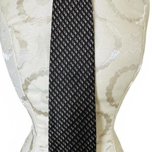 May include: A necktie featuring a dark black and white diagonal chevron or herringbone pattern. The tie is tied in a simple knot at the top and hangs vertically, displaying a consistent geometric texture throughout its length against a neutral background.