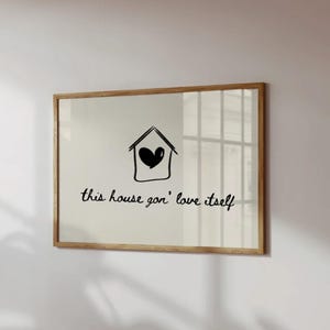 Könnte beinhalten: Ein gerahmter Druck mit einem hellen Holzrahmen. Der Druck zeigt eine schwarze Strichzeichnung eines Hauses mit einem Herz darin und den Satz "this house gon' love itself" in schwarzer Schrift.