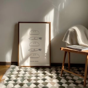 Puede incluir: Un cuadro enmarcado con una ilustración minimalista de panes y peces, con el texto "FEEDS 5000" en la parte inferior. La obra de arte está en un marco de madera marrón, exhibida en una pared sobre una alfombra estampada.