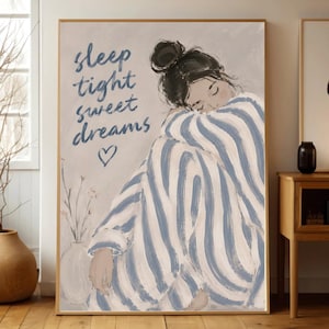 May include: A framed art print features a person in blue and white striped pajamas, curled up and sleeping. The text "sleep tight sweet dreams" is written in blue script above the person, with a heart symbol below. A vase with a plant is in the background.