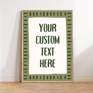 May include: A framed print with the text "YOUR CUSTOM TEXT HERE" in a bold, dark green font. The print has a cream-colored background and is surrounded by a green border with a dotted design. The frame is a light wood color.