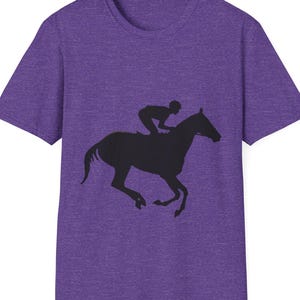 May include: Purple t-shirt featuring a black silhouette of a horse and jockey in motion. The graphic is centered on the front of the shirt. The shirt has a crew neck and short sleeves.