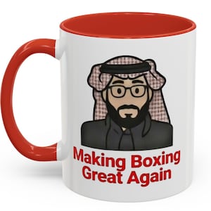 May include: A white ceramic mug with a red interior and handle. The mug features a cartoon illustration of a man wearing a traditional headdress and glasses. The text "Making Boxing Great Again" is printed in red.