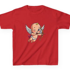 May include: Red t-shirt featuring a cartoon Cupid with wings, a bow and arrow, and a diaper. The Cupid is winking and has a small golden curl on its head. The shirt is made of a soft material.