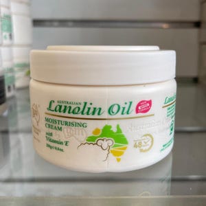 May include: A white jar of Australian Lanolin Oil Moisturising Cream with Vitamin E. The label features green text and a map of Australia. The jar contains 250g of cream and is labeled as a new gentle formula.