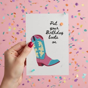 Op de afbeelding: Een wenskaart met een roze achtergrond en confetti. De kaart toont een kleurrijke illustratie van een cowboylaars met de tekst "Put your Birthday boots on."