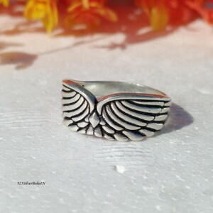 Pu&ograve; includere: Un anello color argento con un design ad ali dettagliato. L'anello presenta una cresta centrale e motivi di piume dettagliati su ogni ala. Il testo "925SilverBohoIN" &egrave; visibile in basso a sinistra.