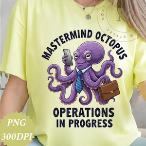 May include: Yellow t-shirt featuring a purple octopus wearing a blue tie and holding a phone and briefcase. The text on the shirt reads "MASTERMIND OCTOPUS OPERATIONS IN PROGRESS."