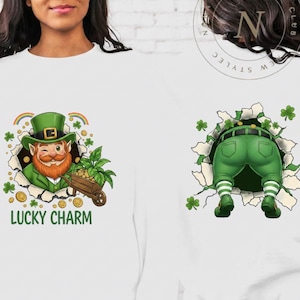 May include: White long-sleeved shirt with two St. Patrick's Day themed graphics. One side features a winking leprechaun with a green hat and beard, the text "LUCKY CHARM", and a rainbow. The other side shows a leprechaun's backside.