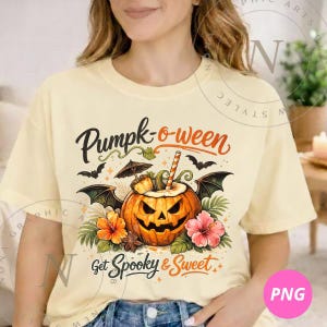 以下が含まれることがあります： クリーム色の半袖Tシャツ。コウモリの羽が生えたジャック・オー・ランタン、南国の花、ストローが描かれたグラフィックが特徴です。黒とオレンジの文字で「Pumpk-o-ween」および「Get Spooky & Sweet」とプリントされています。