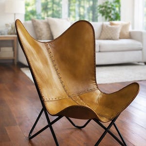 May include: A tan leather butterfly chair with a black metal frame. The chair has a stitched design and a distinctive butterfly shape. The chair is a stylish piece of furniture for a living room or bedroom.