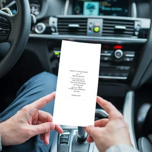 Può includere: Una carta bianca con testo è tenuta davanti al cruscotto di un'auto. Il testo sulla carta recita: "Non ti ho io comandato? Sii forte e coraggioso; non ti spaventare e non ti sgomentare, perché l'Eterno, il tuo Dio, è con te. Giosuè 1:9."